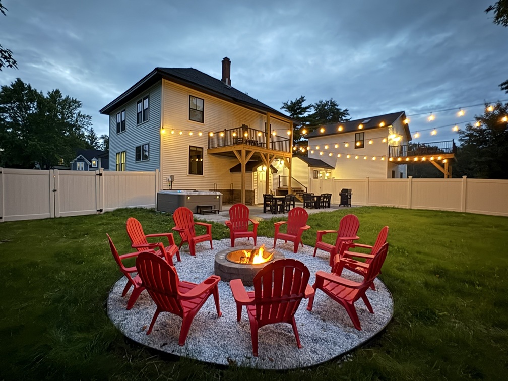 Fenced backyard with fire pit, grill, yard games and bistro lights